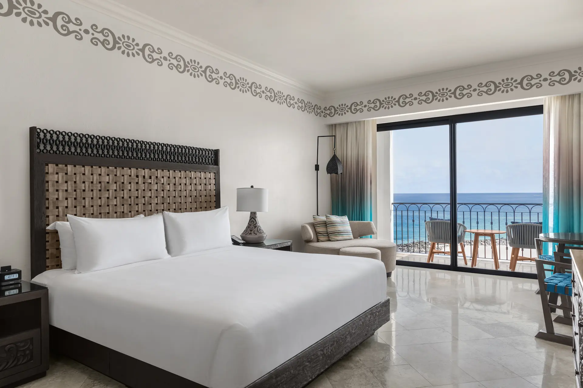Elegant hotel room with king bed, ocean view balcony, modern furnishings, and patterned wall décor.
