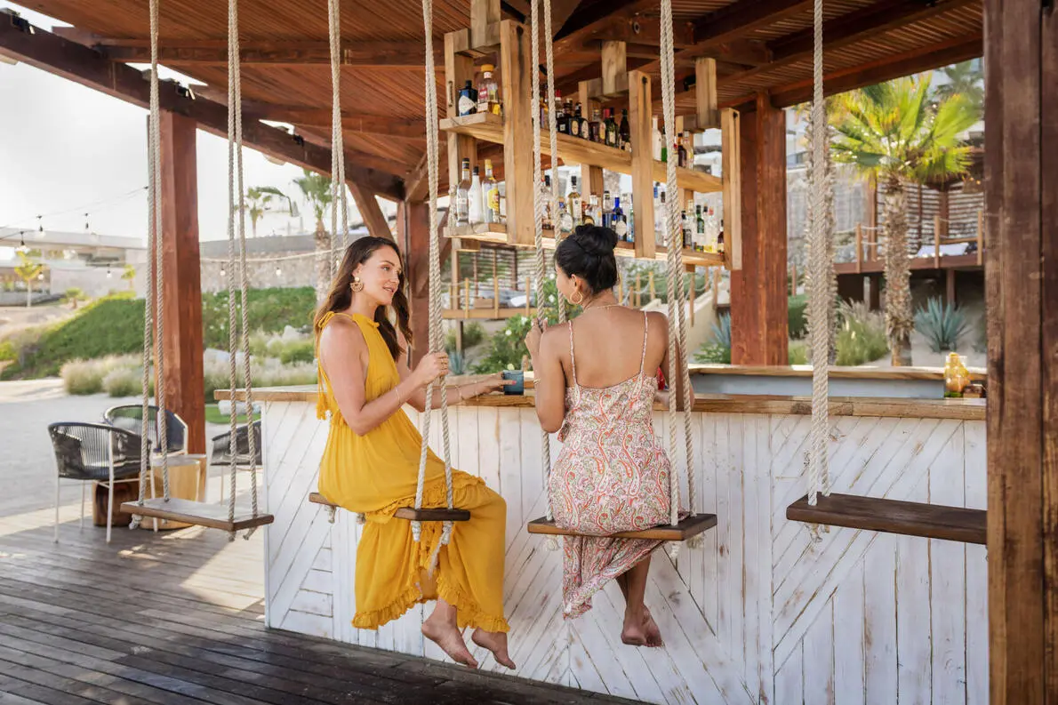 picture of two women sitting on a swing seat in an open bar on the beach