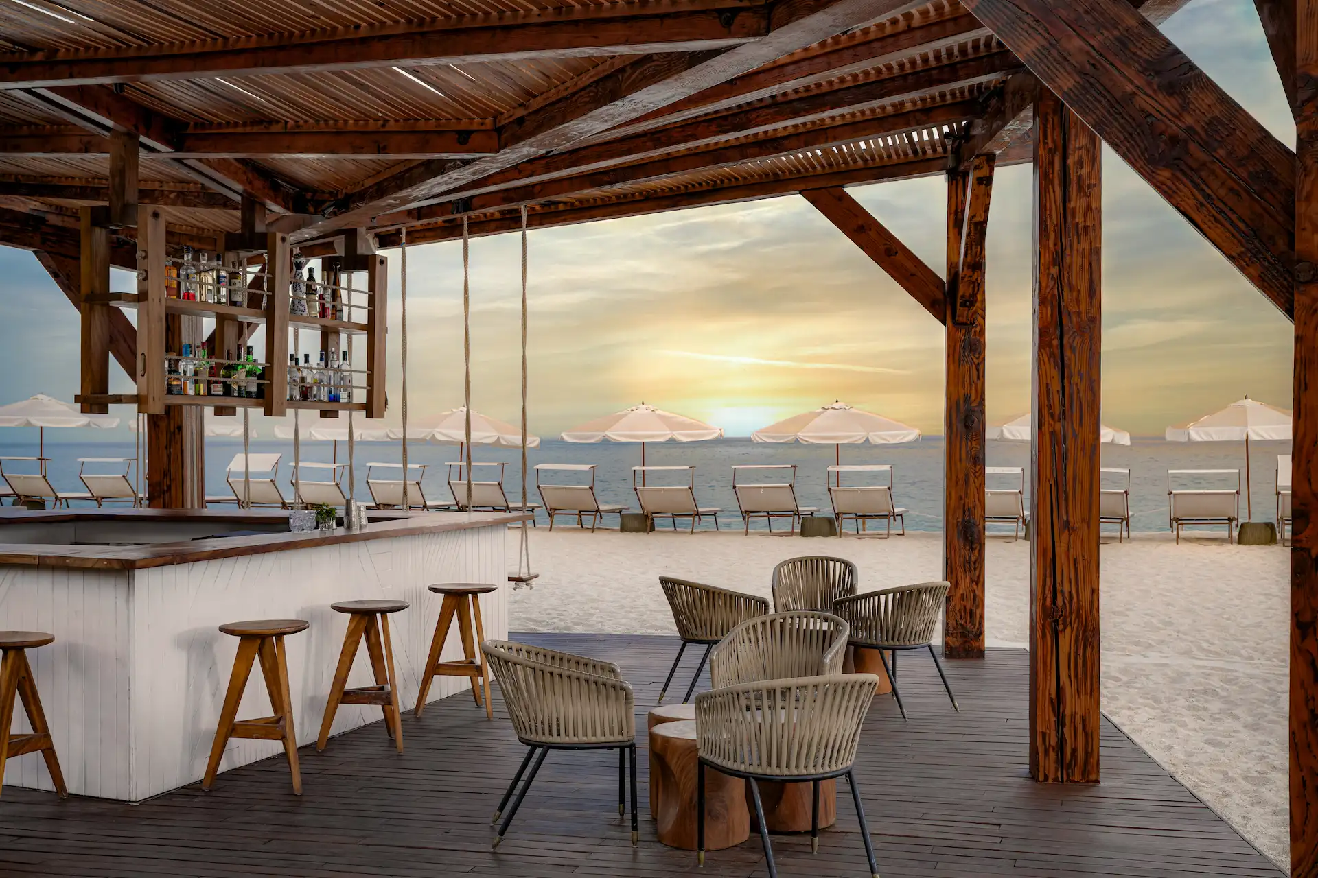 Bar al aire libre frente a la playa con tumbonas frente al atardecer.