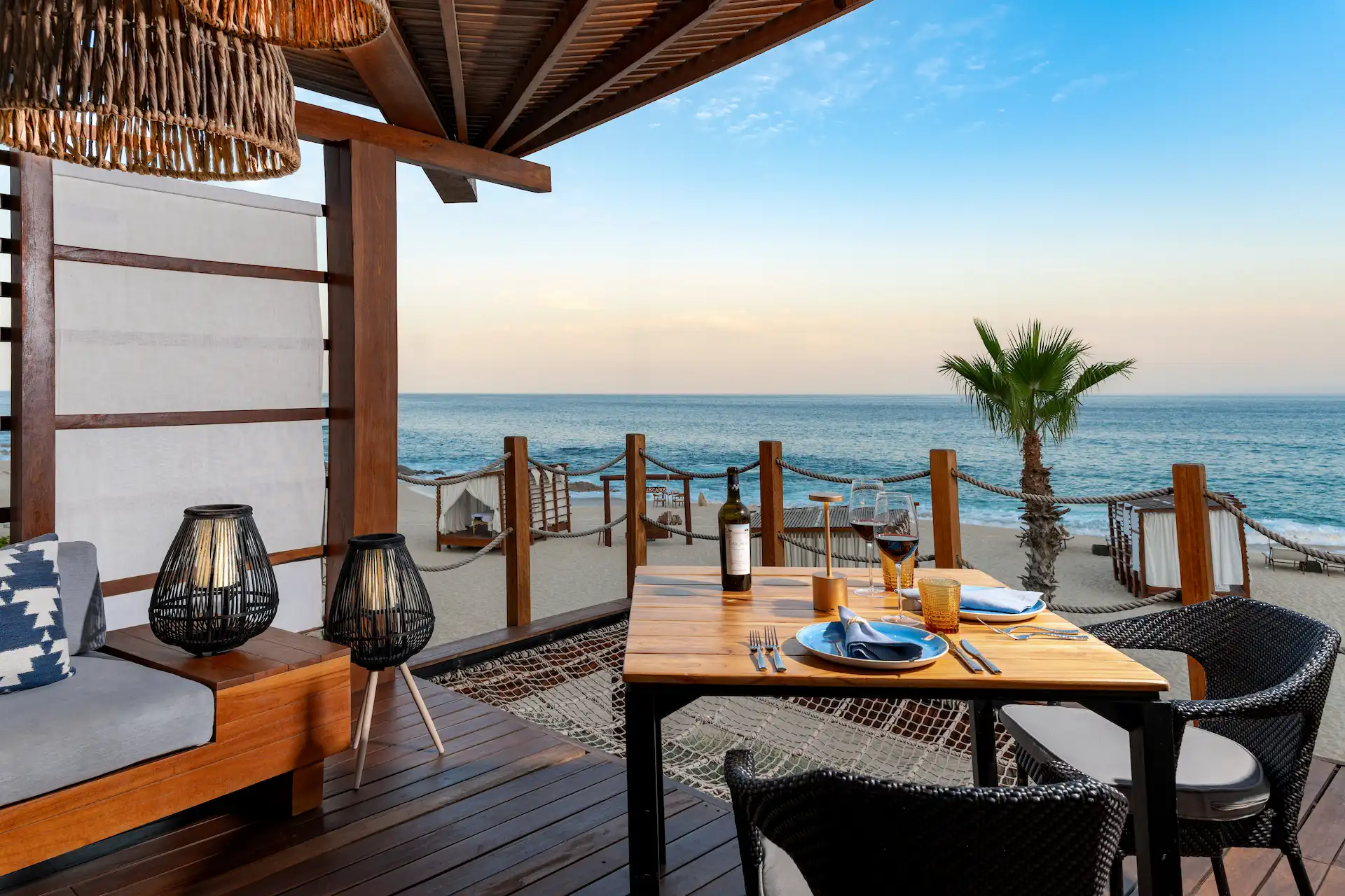 Mesa de comedor en terraza al aire libre con vino y vista al atardecer del océano.