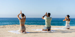 picture of three people doing yoga on beach with sea in front of them