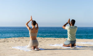 picture of three people doing yoga on beach with sea in front of them