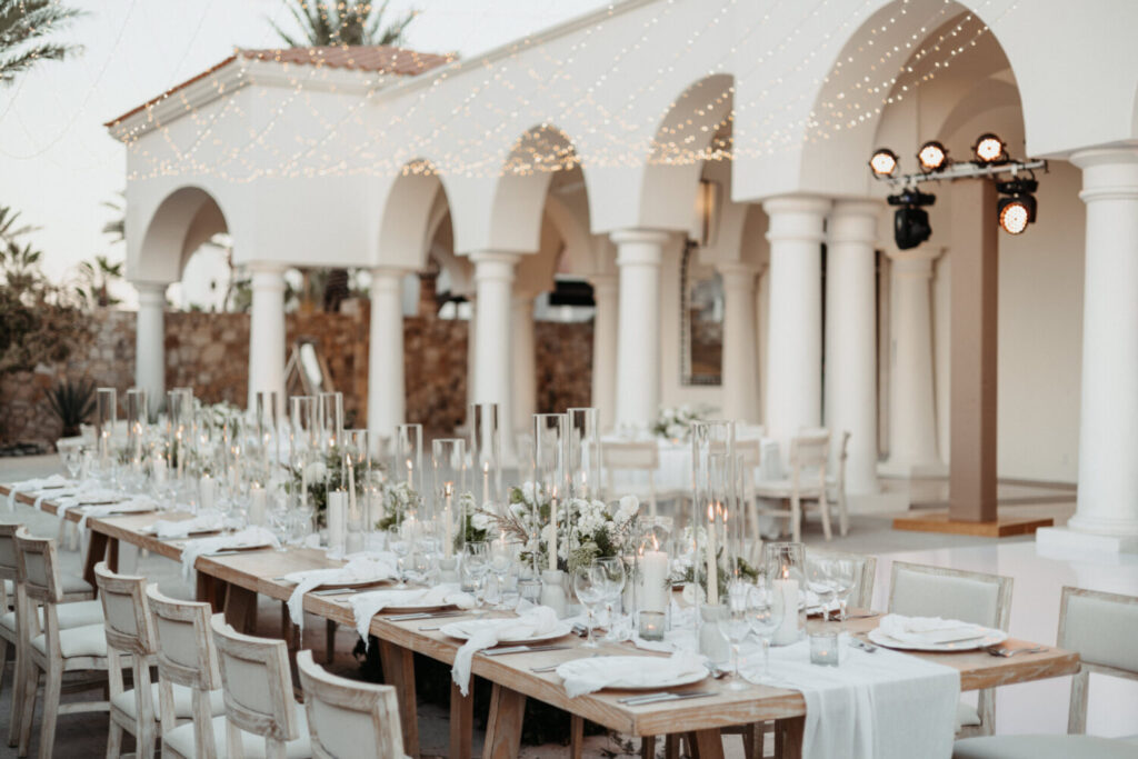 Elegant outdoor wedding reception at Hilton Los Cabos with long wooden tables, white floral décor, candles & string lights.