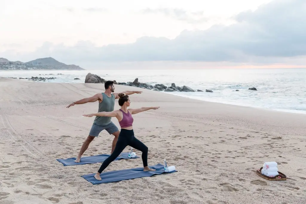 Imagen de dos personas haciendo yoga en la playa con el mar de fondo.