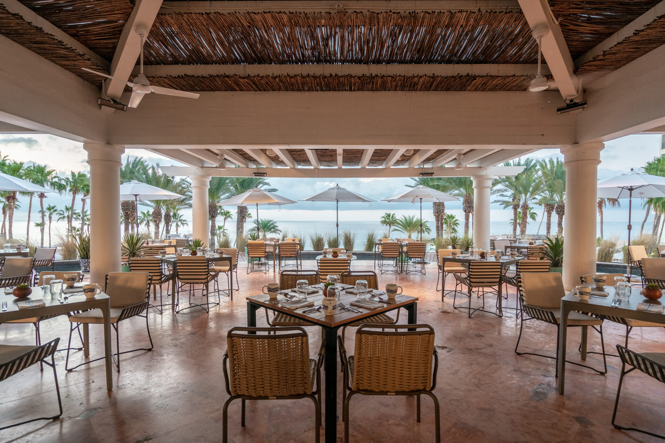 picture of an empty restaurant with table chairs and sea view