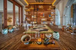 Elegant tasting room with wooden table setup, glassware, pottery, spirits, ladder, and decorative shelves.