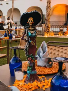 Festive Day of the Dead table centerpiece featuring skeleton figurine in elegant dress and hat.