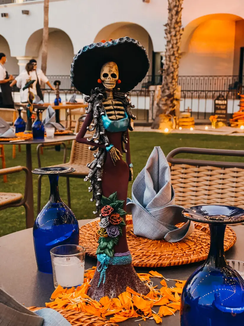 Centro de mesa festivo del Día de Muertos con figura de esqueleto con elegante vestido y sombrero.