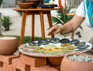 Person prepares colorful tortillas with leaf designs on a plate, surrounded by clay bowls outdoors.