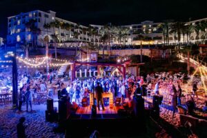 Invitados bailando en la fiesta de Nochevieja en la playa frente al mar del Hilton Los Cabos con luces de guirnalda y un escenario con DJ en vivo.