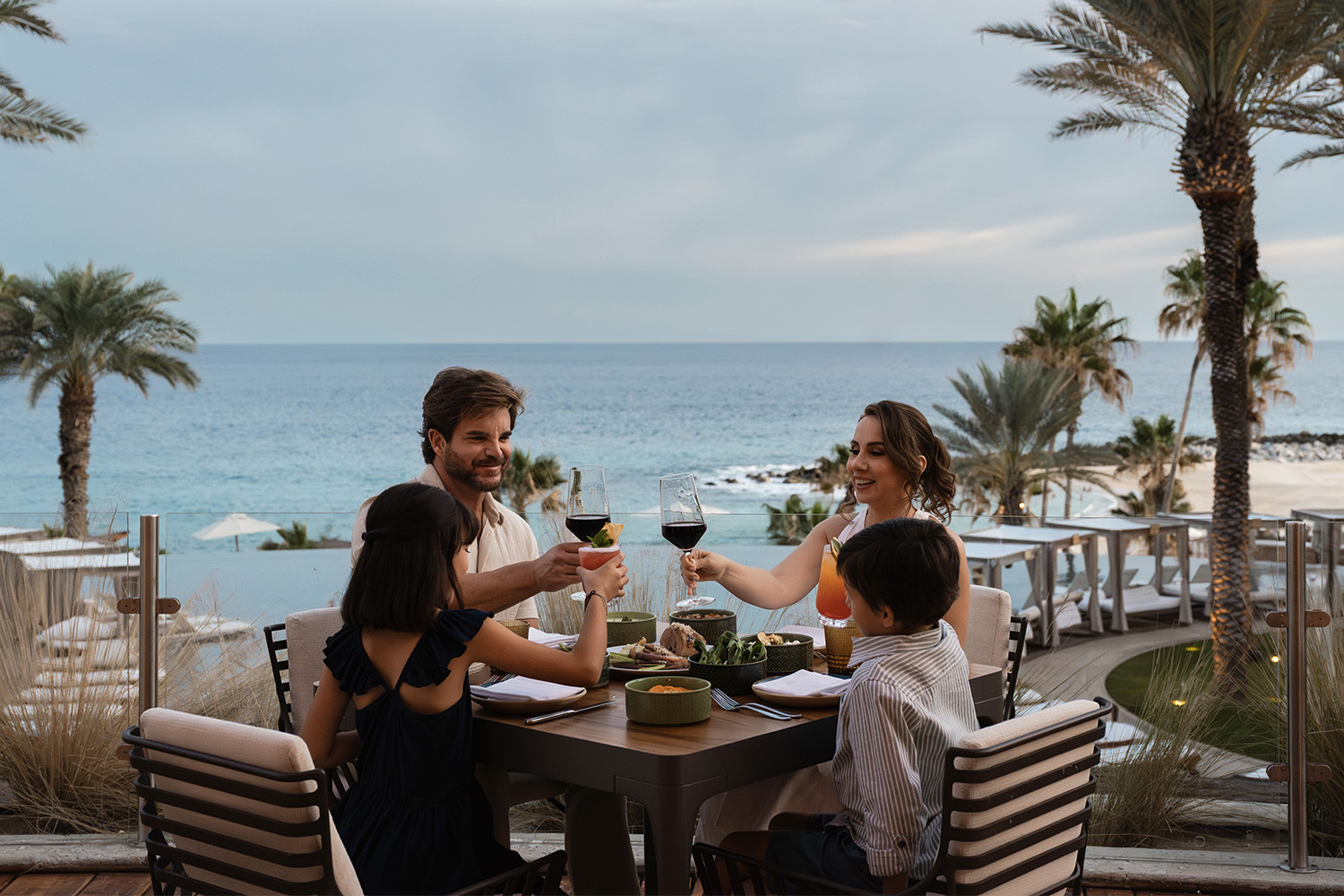 Family toasting with wine and mocktails over an oceanfront dinner at Vela restaurant, Hilton Los Cabos Beach & Golf Resort