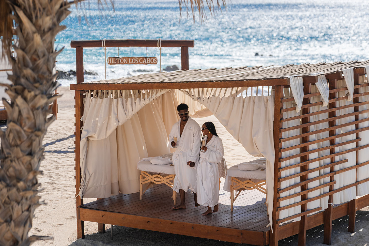 Couple in white robes at an open-air beachfront cabana with two massage tables at hilton los cabos beach & golf resort