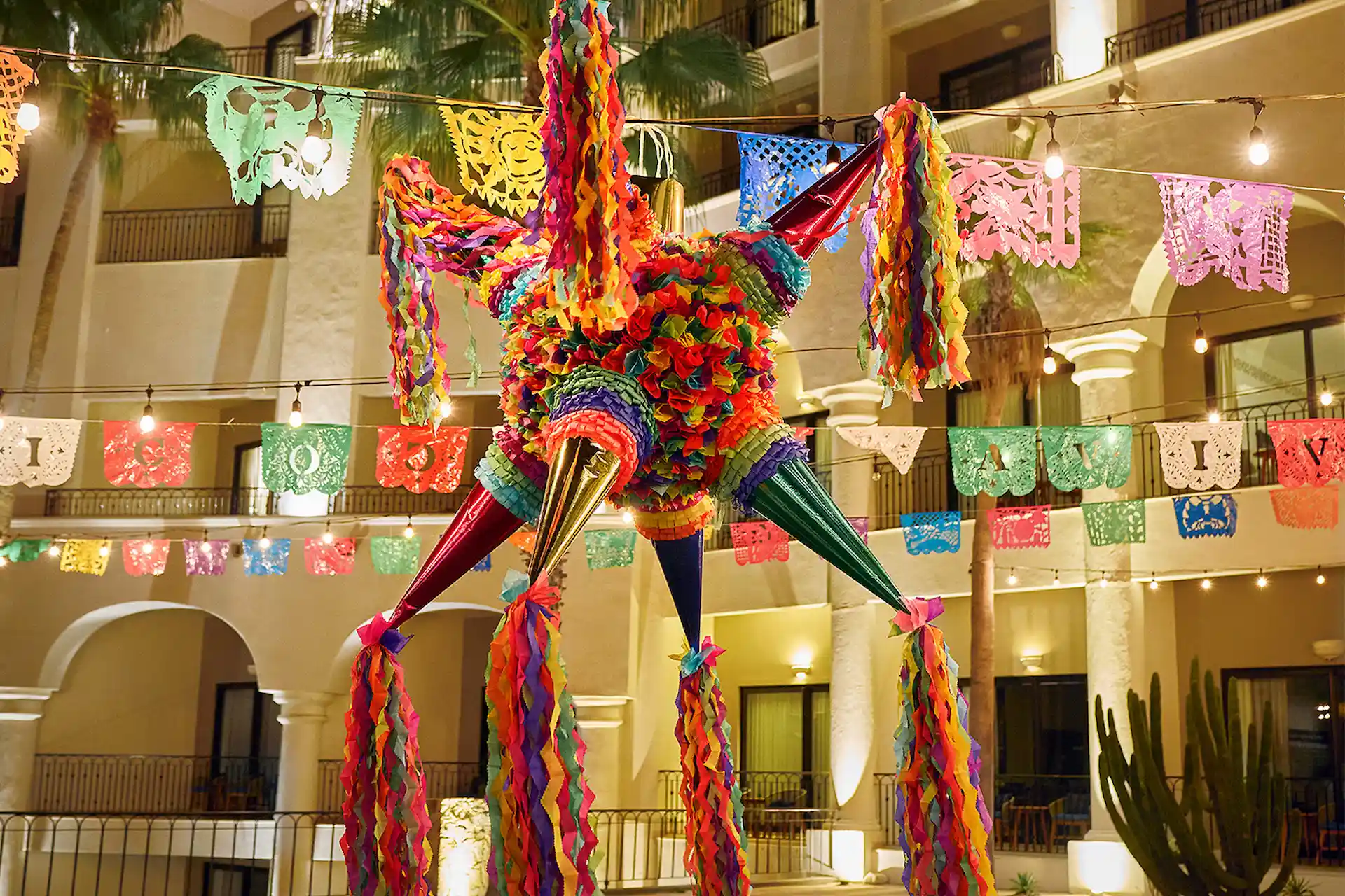 Piñata colorida en forma de estrella colgada en un patio festivo con pancartas de papel picado y cálidas luces de cadena.