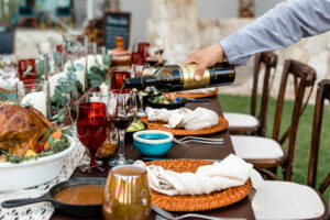 Sirviendo vino tinto a mano en una mesa de comedor al aire libre con pavo asado, velas y decoración de mesa otoñal.