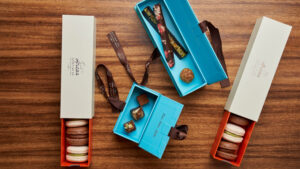 Assorted boxed macarons and chocolates in colorful packaging arranged on a wooden table for elegant presentation.