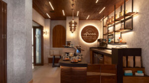 Modern café interior with wooden accents, warm lighting, coffee counter, pastries, and seating area.