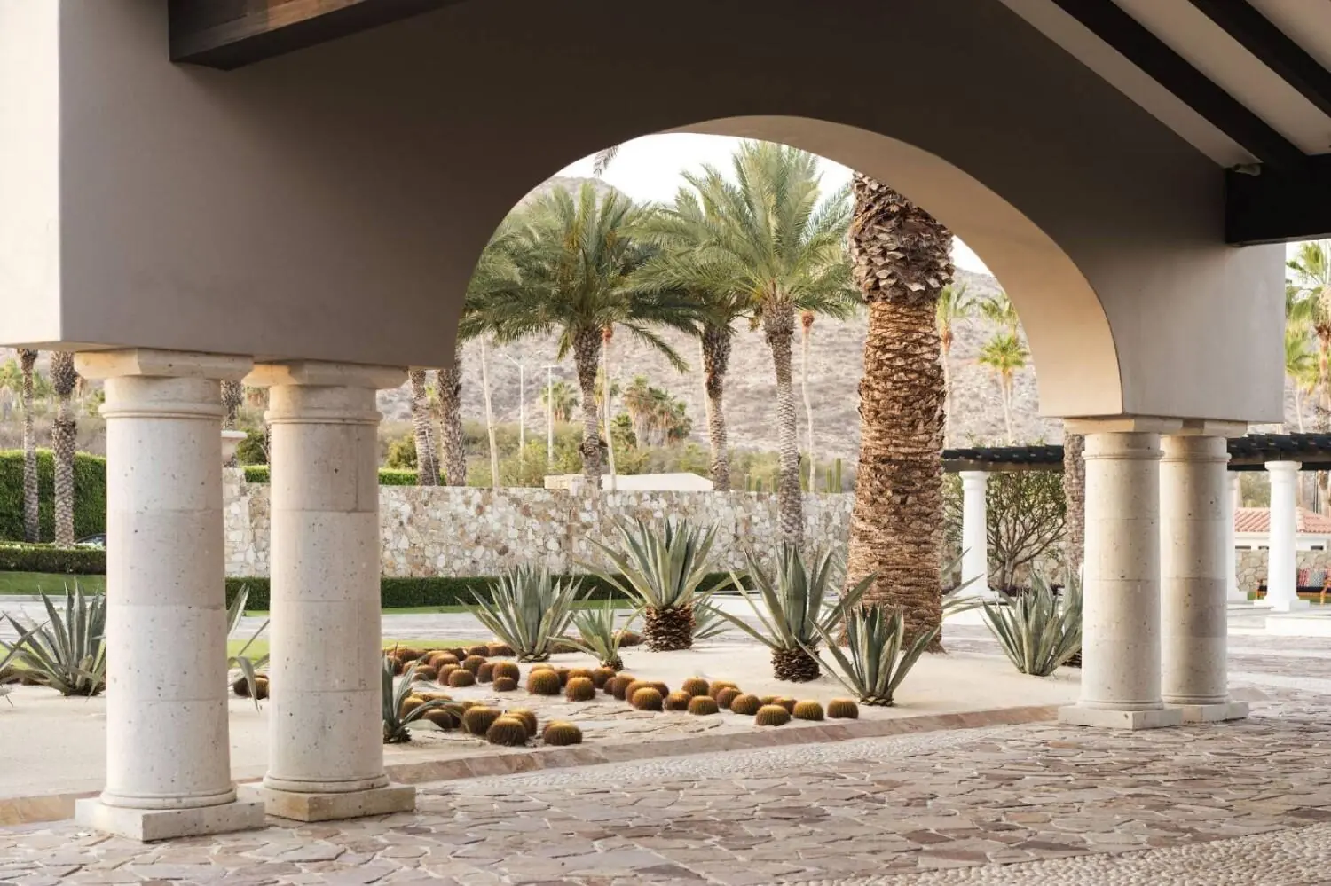 Stone archway with white columns, palm trees, and desert landscaping visible in the background.