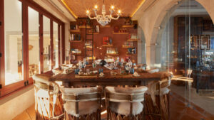 Comedor rústico y elegante en Hilton Los Cabos con lámpara de araña iluminada con velas, sillas tejidas y un acogedor y elegante fondo de bar.