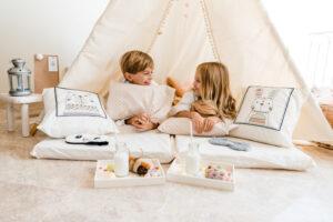 One blonde boy and a blonde girl having fun in a tipi tent