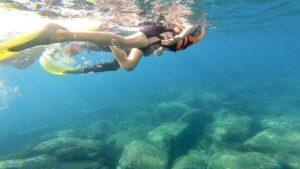 Two people snorkeling underwater above rocks in clear blue ocean water.