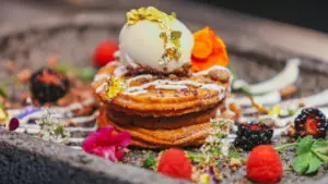 Gourmet plated dessert with ice cream, edible gold, berries, flowers, colorful sauces and elegant garnishes.