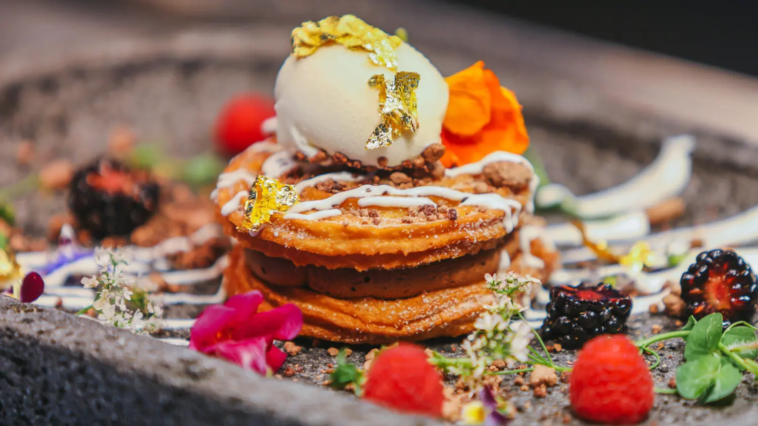Postre gourmet chapado con helado, oro comestible, frutos rojos, flores, salsas coloridas y elegantes guarniciones.