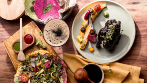 Coloridos platos gourmet mexicanos, que incluyen ensalada, salsas, bebidas y plato principal, dispuestos artísticamente en una mesa de madera.