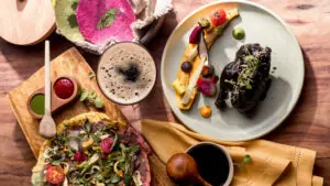 Colorful gourmet Mexican dishes, including salad, sauces, drinks, and entree, arranged artfully on a wooden table.