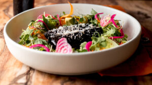 Ensalada colorida con verduras, rodajas de rábanos, aguacate y hamburguesa de frijoles negros servida en un recipiente de cerámica blanca.