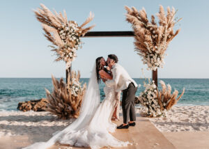 a bride in white dress kissing the groom at the beach
