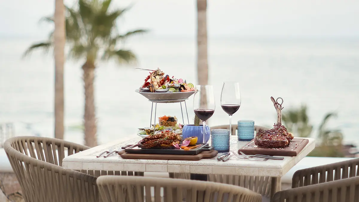 Elegant oceanview dining at Hilton Los Cabos with gourmet dishes, wine, and tropical ambiance under swaying palms