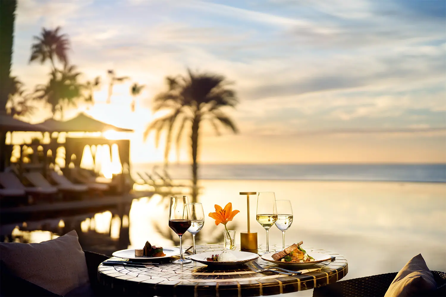 Sunset dining by the pool at Hilton Los Cabos with gourmet plates, wine, and ocean views in a tropical, serene setting.