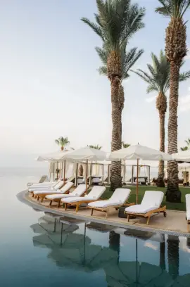 Infinity poolside at Hilton Los Cabos with cushioned loungers, umbrellas, and palm trees under a clear tropical sky.