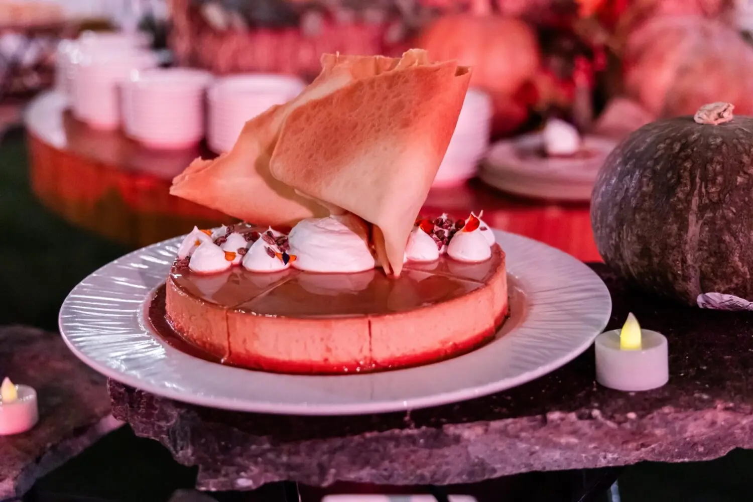 Tarta de queso y caramelo cubierta con crema batida, flores comestibles, decoración de tejas crujientes, en un plato blanco.