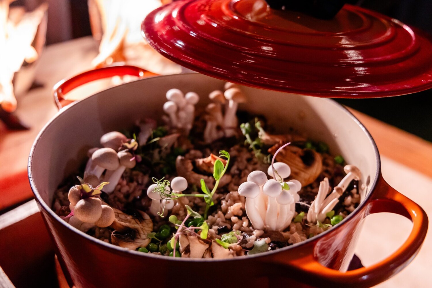 Close-up of gourmet mushroom risotto in red pot, topped with fresh herbs and vegetables.