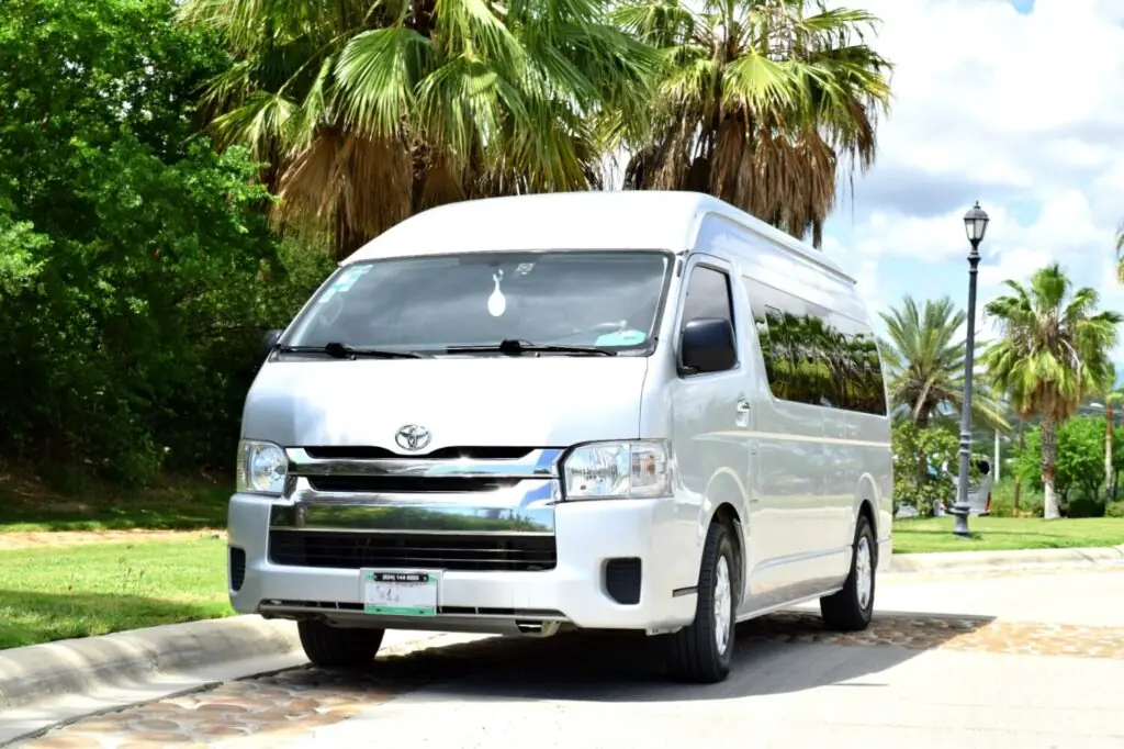 Silver Toyota passenger van parked on a sunny, palm-lined road in a tropical outdoor setting.