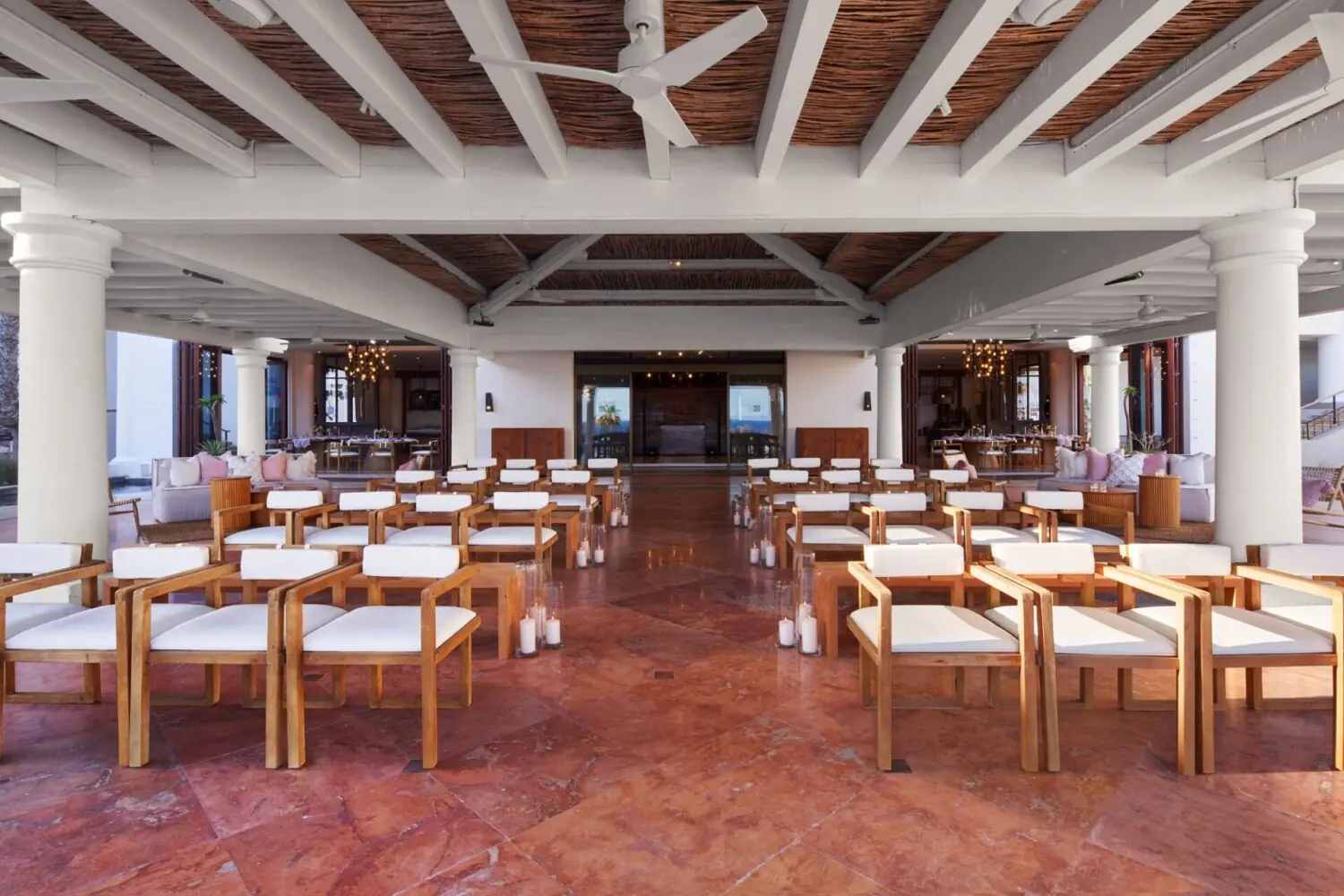 Indoor wedding ceremony setup with wooden chairs arranged in rows, candles lining the aisle, open-air design.