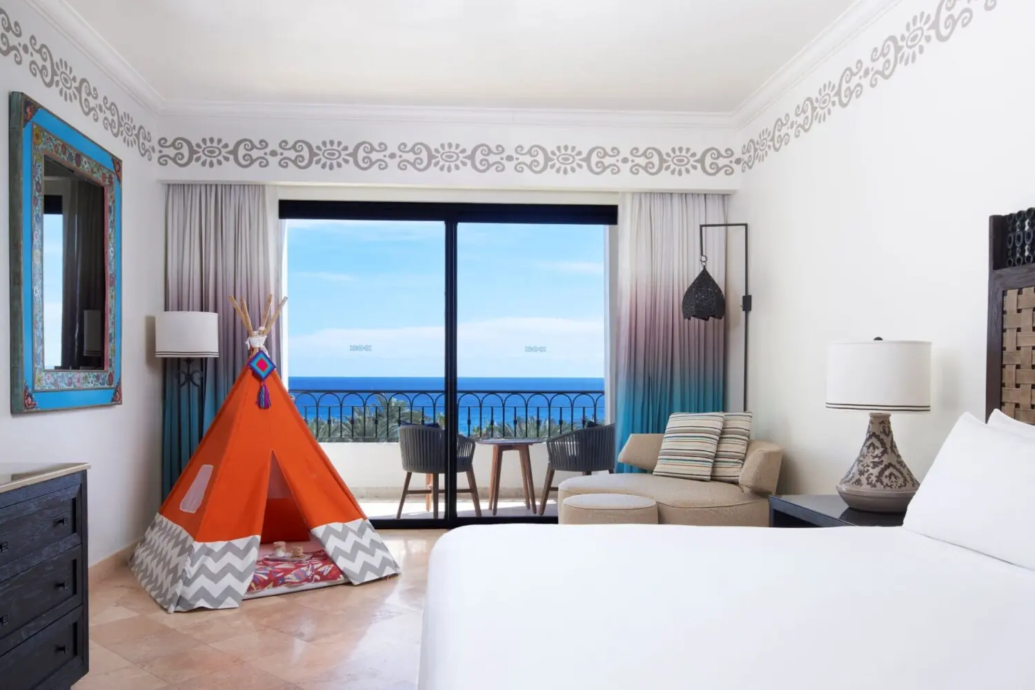 Habitación de hotel luminosa con tipi para niños, zona de estar y balcón con vista al océano.