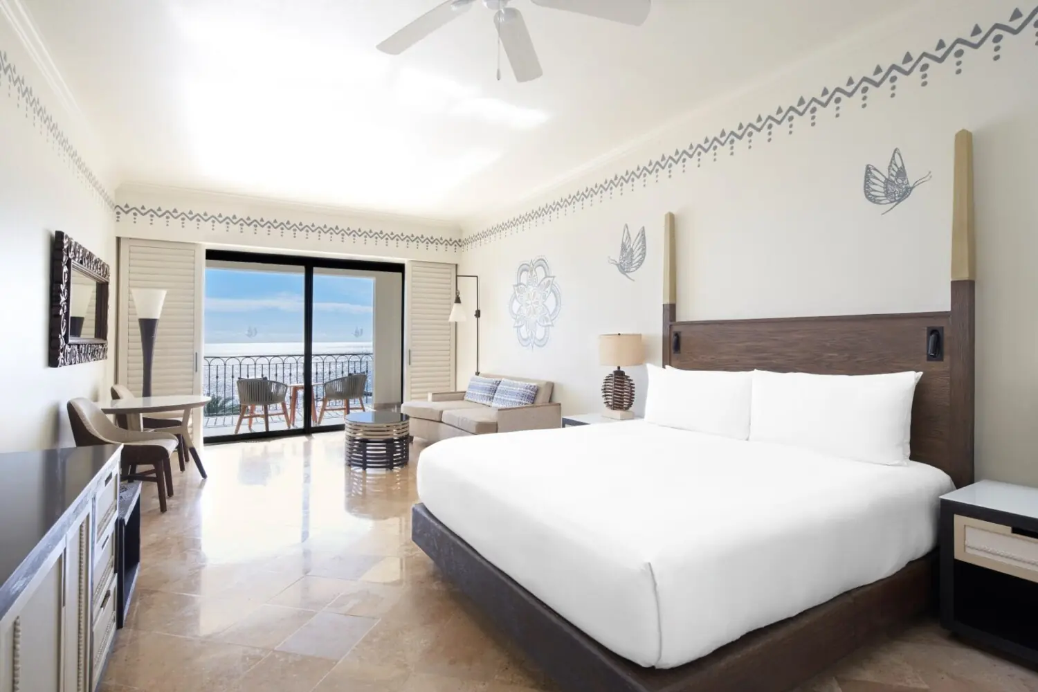 Habitación de hotel moderna y luminosa con cama grande, balcón con vista al mar y elegante mobiliario minimalista.