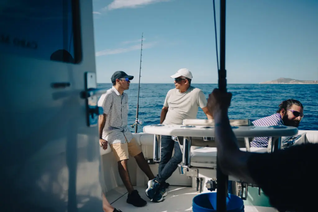 Group of men relaxing and chatting on a fishing boat at sea under clear blue skies.