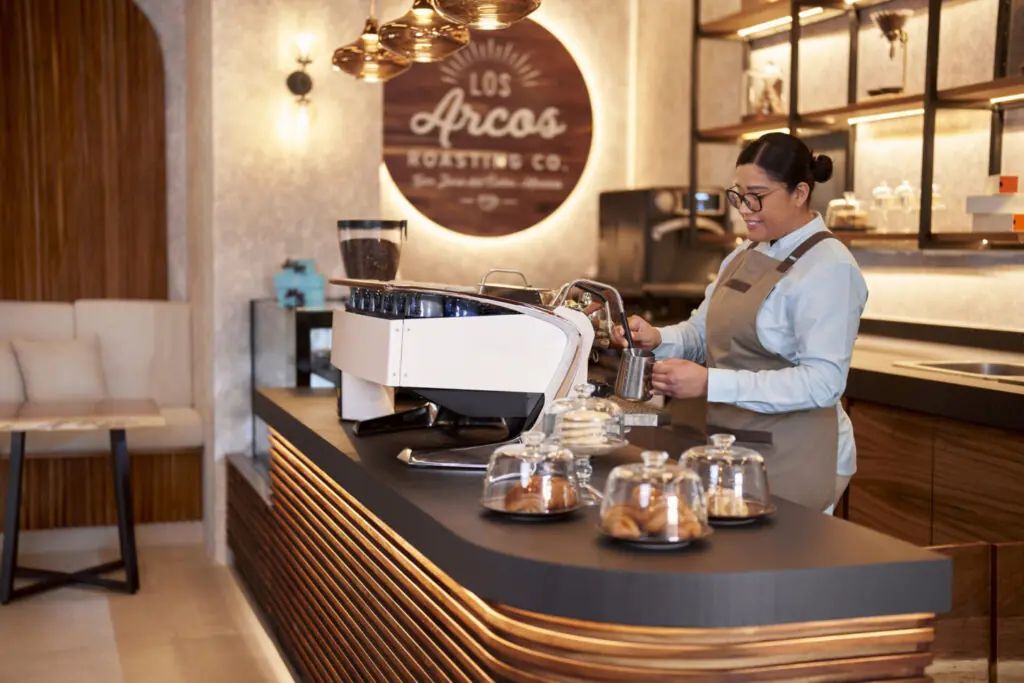 Barista preparing espresso behind a modern coffee counter with pastries displayed in a warm, stylish café.