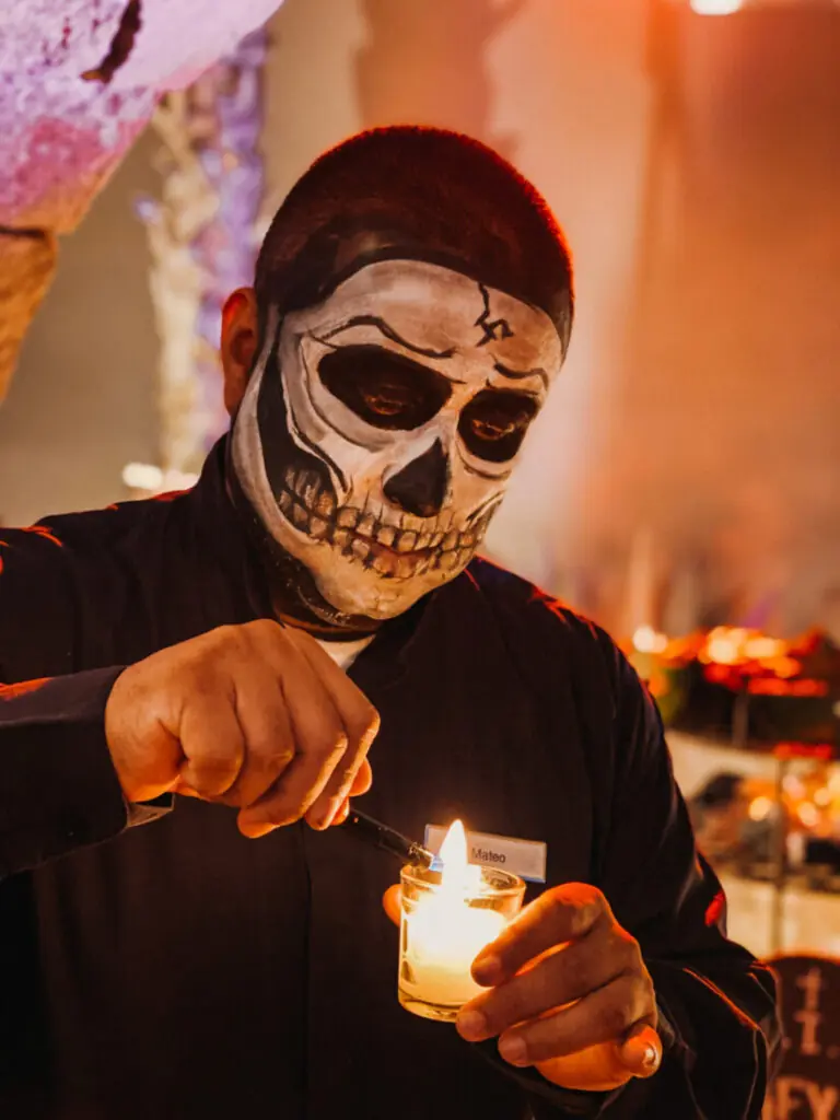 Person with skull face paint lighting a candle at a dimly lit event or celebration.