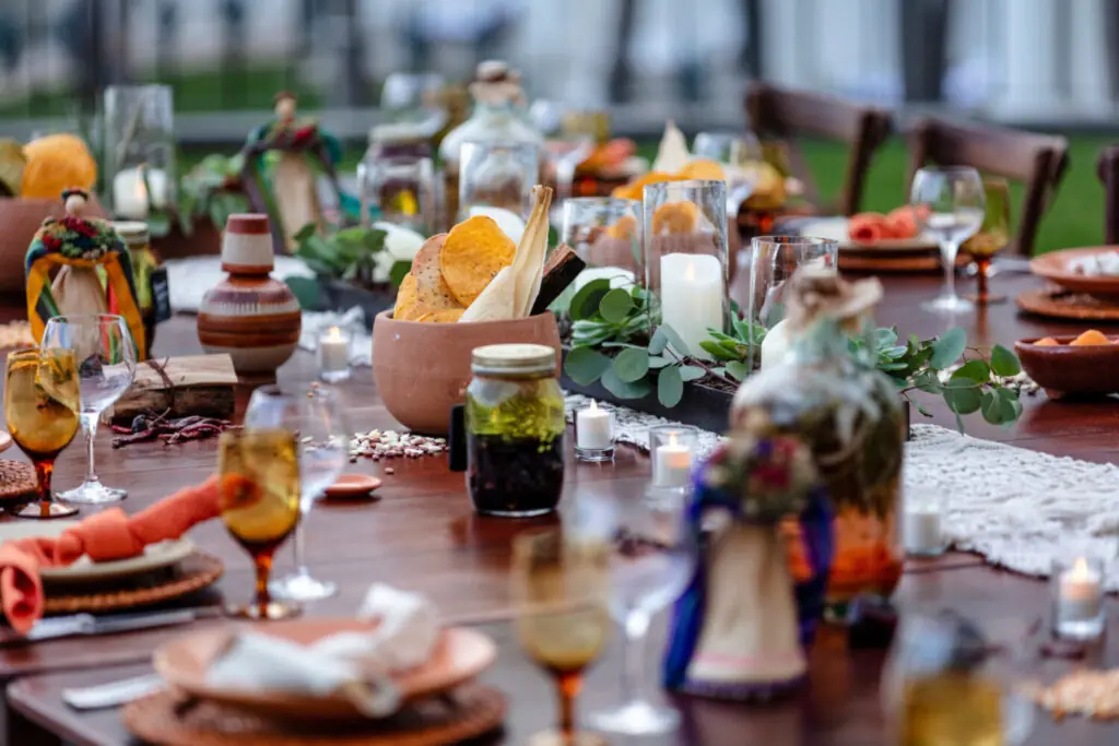 Outdoor dining table set with candles, glassware, greenery, and shared dishes, creating a warm, festive atmosphere.