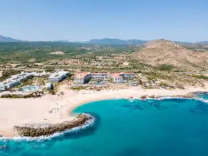 Aerial view of a beachfront resort with turquoise water, sandy shore, and mountains in the background.