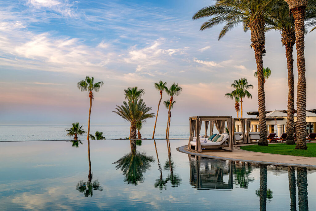 Infinity pool overlooking the ocean with palm trees, cabanas, and lounge chairs at a luxury beachfront resort.