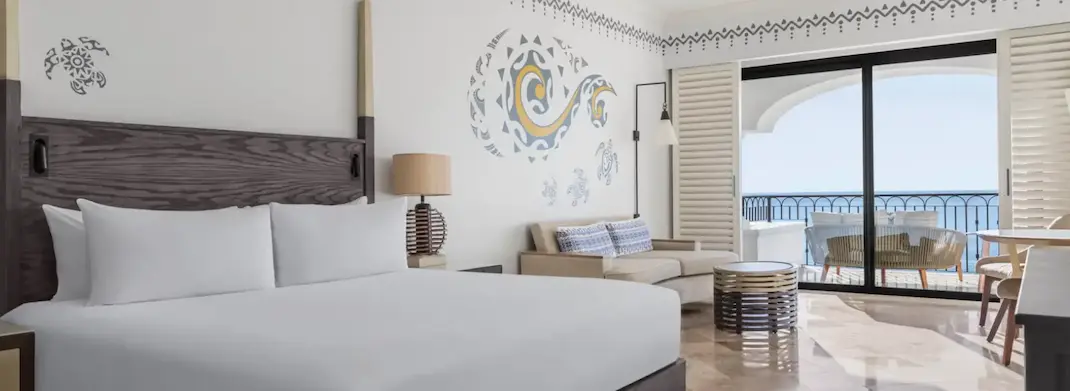 Modern hotel room with king bed, decorative wall art, and balcony overlooking the ocean