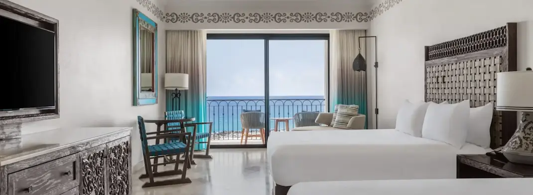 Ocean-view hotel room with two beds, balcony seating, and natural light.