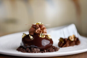 Elegante postre de chocolate cubierto con pan de oro, remolino de crema y nueces en un plato blanco.