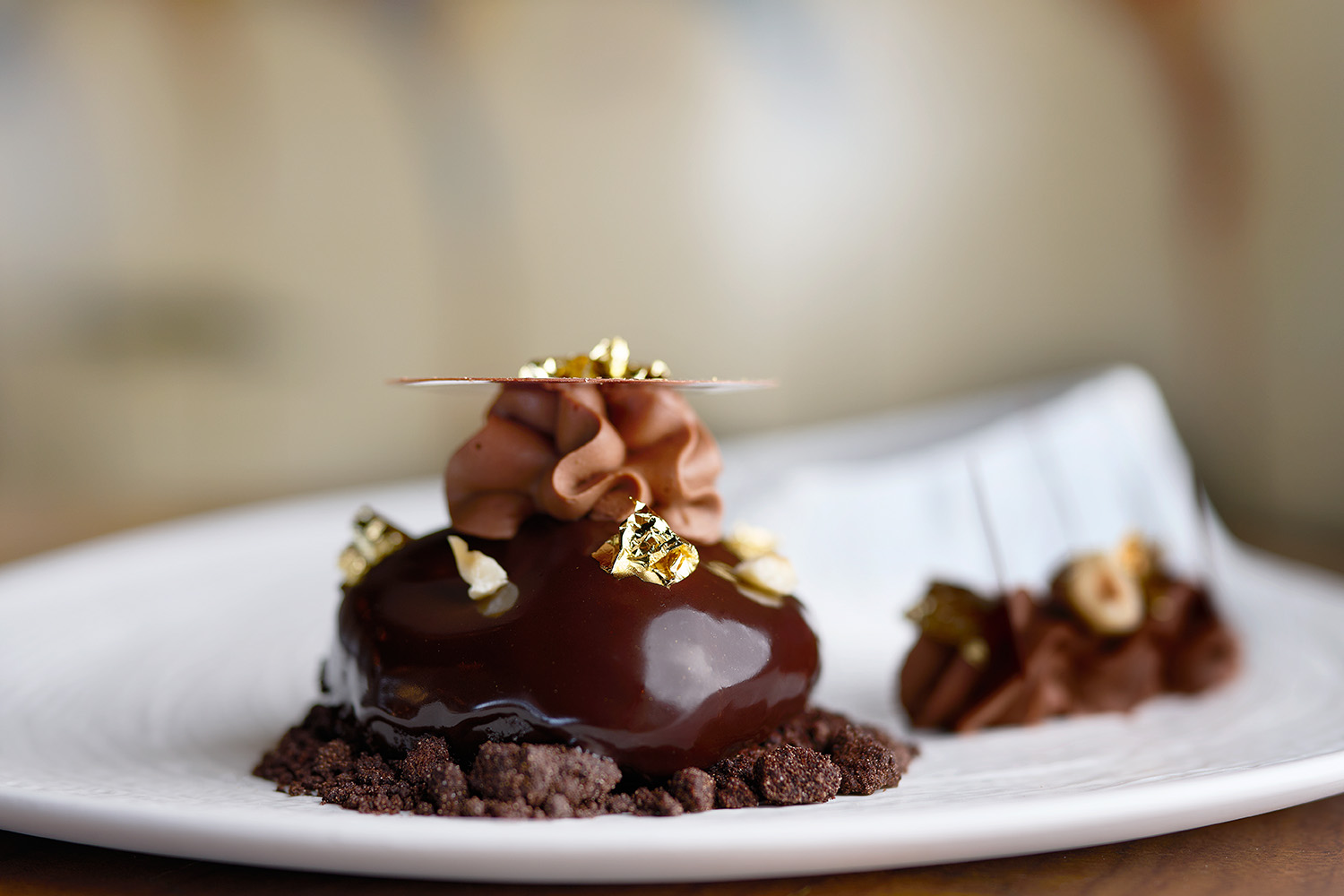 Elegante postre de chocolate cubierto con pan de oro, remolino de crema y nueces en un plato blanco.