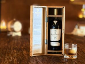A bottle of The Macallan 25-year-old single malt whisky in a wooden case beside a glass on a table.